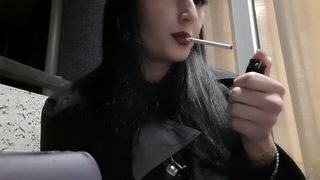 Dominatrix Nika smokes a cigarette on the balcony. Mistress sexy red lips blow smoke in your face